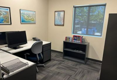 Bright private office suite with an L-shaped desk, computer monitor, and bookshelves.