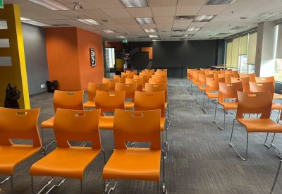 Large training room with rows of orange chairs facing a dark feature wall.