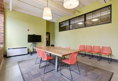 Casual meeting room with a wooden table, orange chairs, and a mounted flat-screen TV.