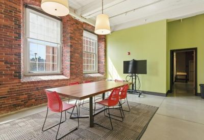 Bright conference room featuring a large wooden table, red chairs, and tall windows.