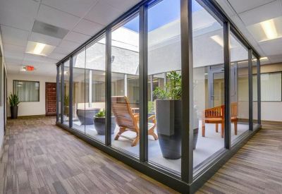 Glass-walled indoor courtyard with wooden seating and potted plants.