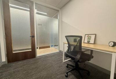 Private one-person office with a light wood desk, mesh chair, and frosted glass door.