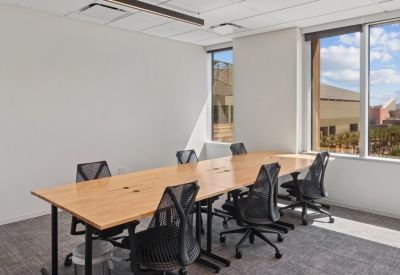 Bright workspace featuring a long wooden communal table and ergonomic mesh chairs.