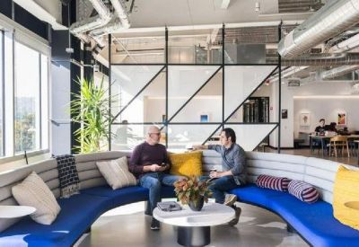 Sunlit communal lounge with a curved blue sofa and colorful accent pillows.