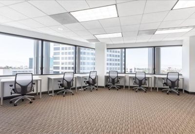 Bright coworking area with rows of desks and mesh chairs against large windows.
