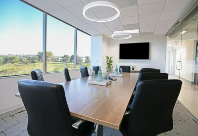 Bright conference room with a large wooden table, black leather chairs, and floor-to-ceiling windows.