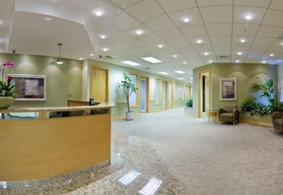 Bright reception lobby with a curved wood desk, potted orchids, and recessed lighting.