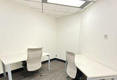 Minimalist two-desk office with white furniture and a frosted glass wall.