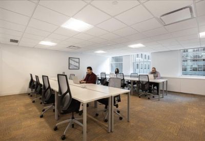 Spacious open-plan workspace with rows of long white desks and ergonomic mesh chairs.