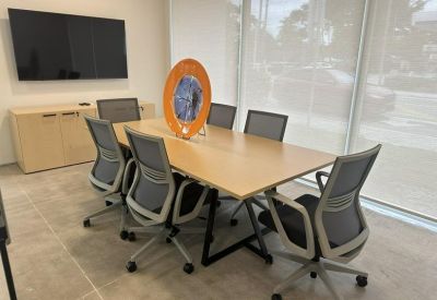 Professional meeting room featuring a light wood table, grey mesh chairs, and a large wall-mounted screen.