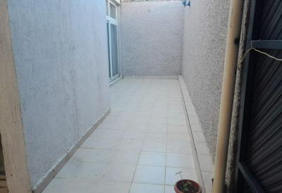 Long outdoor tiled patio area with high walls and glass door access.