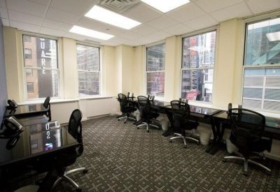 Open-plan workspace with a long row of desks beside windows and patterned carpeting.