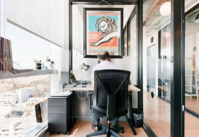 Private glass-walled office suite with a single desk, ergonomic chair, and colorful wall art.