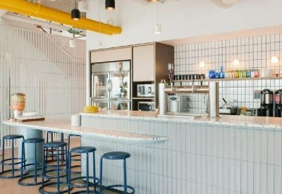 Modern office kitchen featuring a white tiled backsplash, breakfast bar with blue stools, and coffee station.