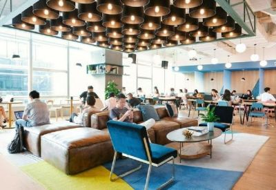 Large coworking lounge area under a decorative ceiling light installation with varied seating and blue accents.