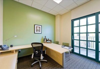 Bright private corner office with a green feature wall and large window.