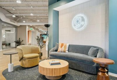 Modern lounge area with a curved gray sofa, yellow armchair, and neon logo on a feature wall.