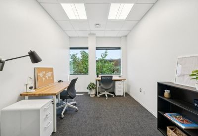 Bright internal two-person office suite with white desks and large windows showing greenery.