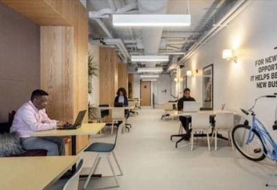 Coworking corridor with individual workstations, light wood accents, and a blue bicycle.