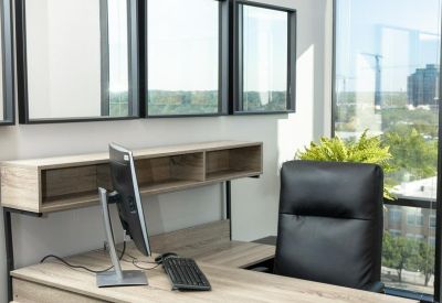 Private corner office with a wooden L-shaped desk and large windows.