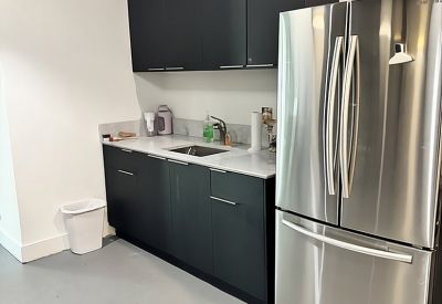 Sleek modern kitchenette with dark cabinetry and a large stainless steel refrigerator.