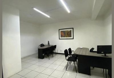 Open office area featuring multiple black desks, computers, and tiled flooring.