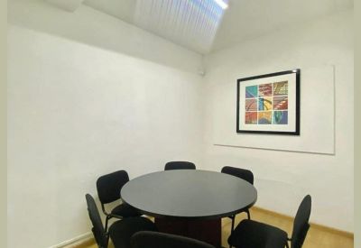 Bright meeting room with a round black table, six chairs, and a skylight.