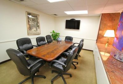 Professional boardroom with a long wood table and black leather chairs.
