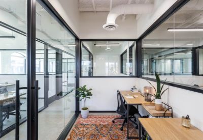 Private office suite with glass walls, a wooden desk, and a colorful patterned rug.