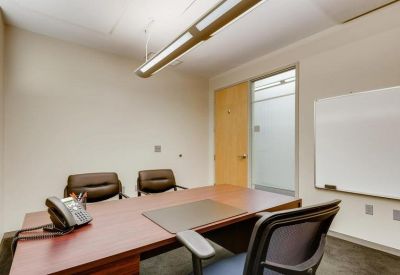 Private office featuring a wooden desk, two guest chairs, and a whiteboard.