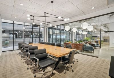Modern boardroom with a light wood table, black leather chairs, and globe pendant lighting.