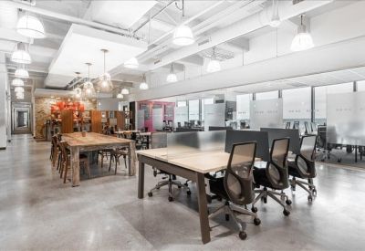Spacious coworking area with long wooden tables, ergonomic chairs, and modern pendant lighting.