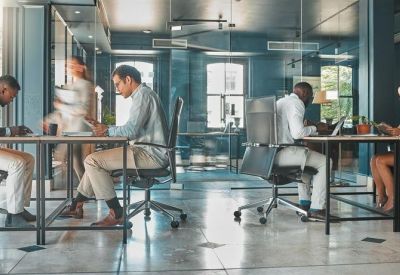 Modern office interior with glass partitioning and people working at shared desks.