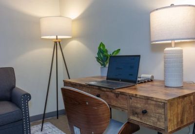 Detail of a wooden desk setup featuring a laptop and modern desk lamp next to a dark armchair.