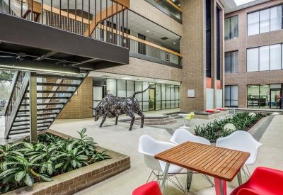 Modern communal atrium featuring a bronze bull sculpture, indoor plants, and colorful seating.