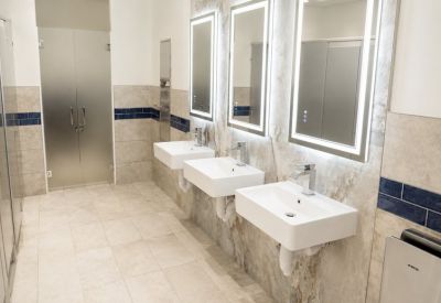 Modern restroom with floating white sinks, backlit mirrors, and blue tile accents.