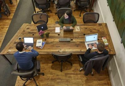 Overhead view of a rustic communal wood table where people work on laptops.