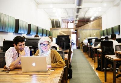 Wide-angle view of a bustling open-plan workspace with rows of desks and industrial lighting.