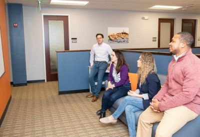 Team members relaxing and talking on a blue sofa in a comfortable office lounge area.