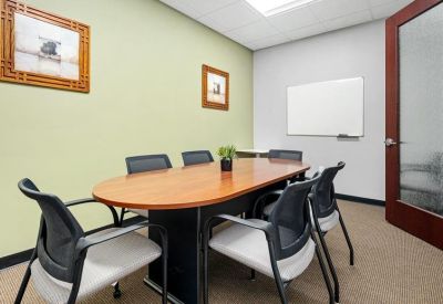Bright conference room featuring an oval wood table, mesh chairs, and a whiteboard.