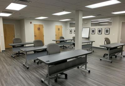 Classroom-style meeting room with rows of grey desks and a whiteboard.