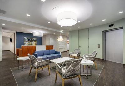 Bright reception lounge with blue sofa, armchairs, and elevator access.