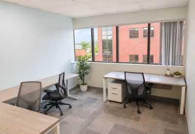Bright two-person office suite with L-shaped desks and large windows.