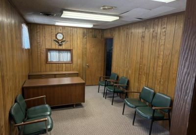 Traditional reception or waiting area with wood paneling and green vinyl chairs.