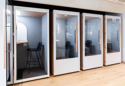 Row of private acoustic phone booths with glass doors and comfortable seating.