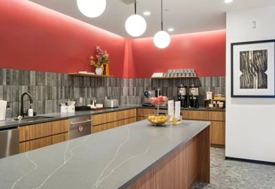 Modern kitchen and breakroom area with gray tile backsplash and warm wood cabinetry.