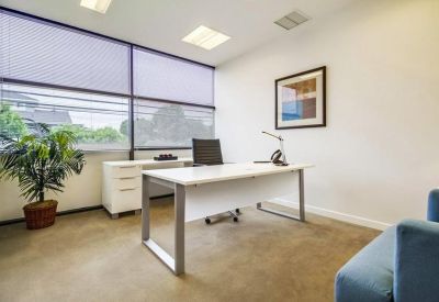 Private office suite with a large white desk, potted plant, and window blinds.