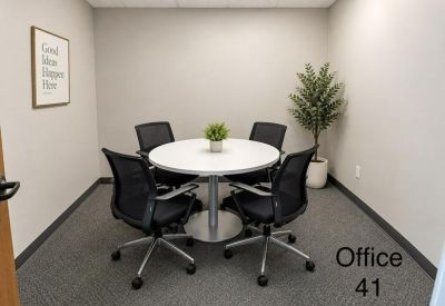 Four-person meeting room with a round white table and black mesh chairs.
