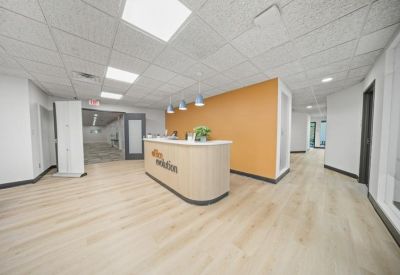Reception area with a light wood desk, orange feature wall, and modern lighting.