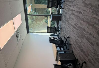 Office space with several black mesh chairs and light wood desks beside a window.